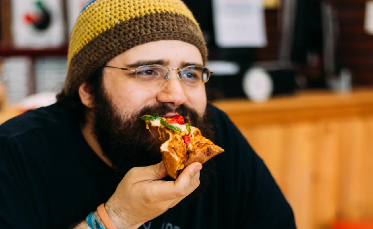 A man wearing cap and eating pizza slice