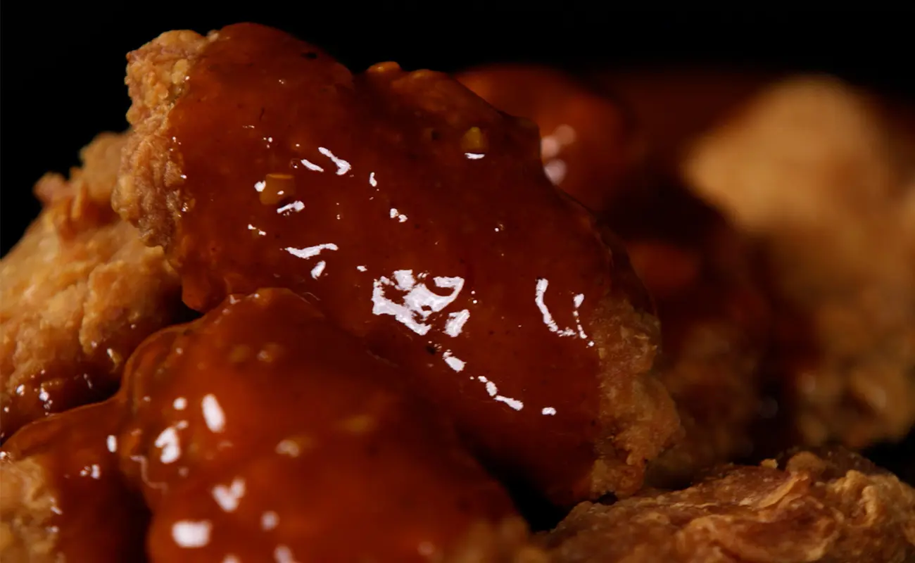 Close-up of crispy fried chicken wings coated in a thick, glossy, reddish-brown sauce, highlighting their crunchy texture and rich flavor.