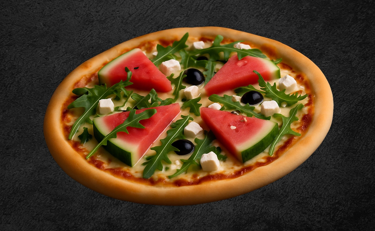Creative pizza topped with fresh watermelon slices, arugula leaves, feta cheese cubes, and black olives on a dark background.