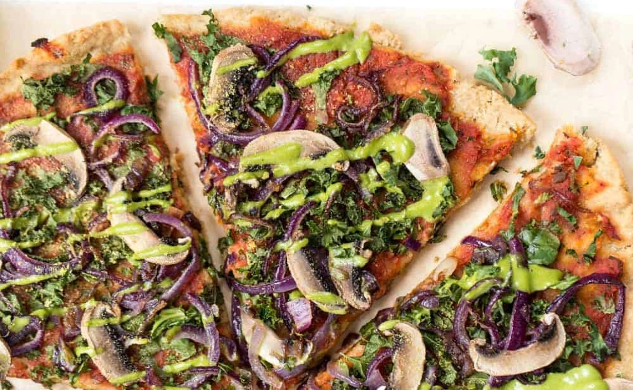 Healthy vegetarian pizza with mushrooms, kale, red onions, and green pesto drizzle on crispy crust